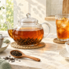 茶葉が開いたガラスのティーポットと広い茶こし、紅茶のカップとアイスティー