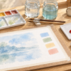 水彩紙の試し塗りとパレット、水入れ、筆、アクリル絵の具を並べた机のイラスト